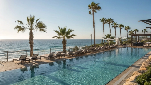 Resort swimming pool overlooking Mediterranean Sea with palm trees and loungers